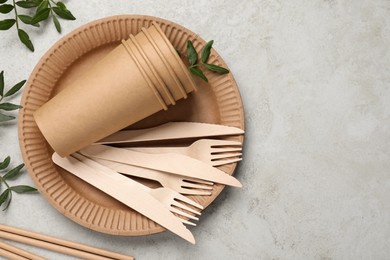 Photo of Disposable tableware and green twigs on light background, flat lay. Space for text