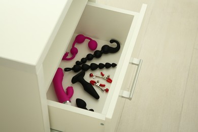 Photo of Many different sex toys in open drawer of nightstand indoors, closeup. Space for text