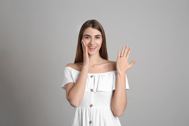 Photo of Happy young woman wearing beautiful engagement ring on grey background