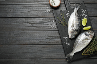 Raw dorada fish on black wooden table, flat lay. Space for text
