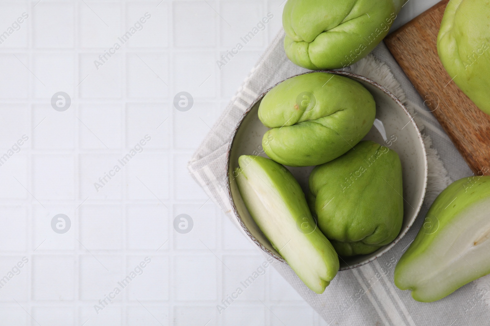 Photo of Cut and whole chayote in bowl on white tiled table, flat lay. Space for text