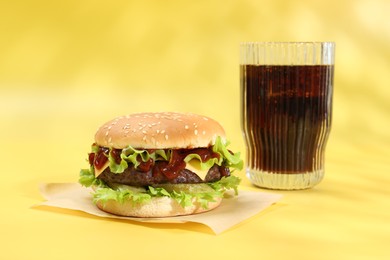 Photo of Burger with delicious patty and soda drink on yellow background