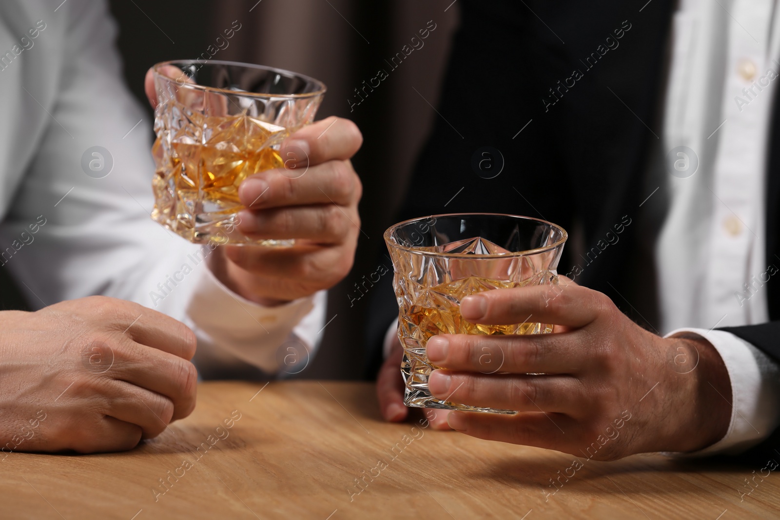 Photo of Men with glasses of whiskey at wooden table indoors, closeup