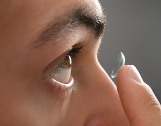 Young man putting contact lens into his eye, closeup