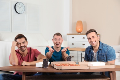 Group of friends with tasty food laughing while watching TV at home