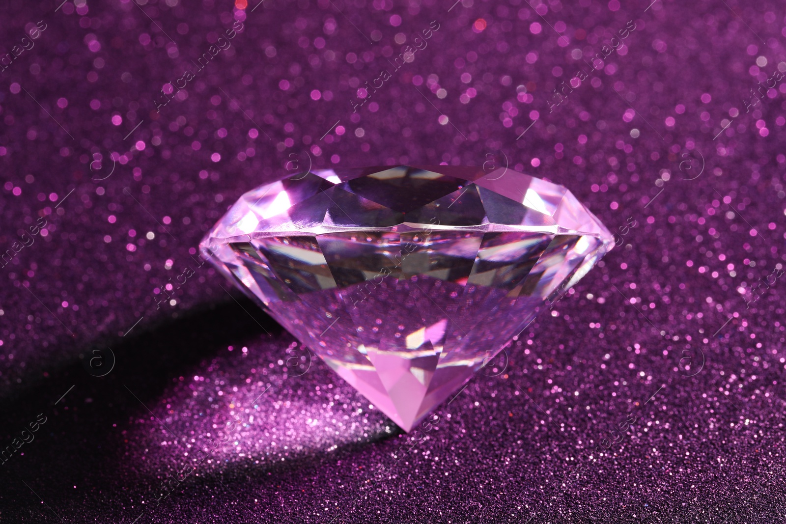 Photo of Beautiful shiny diamond on purple glitter background, closeup