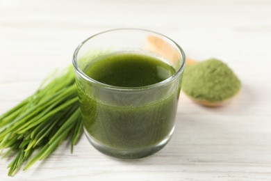 Wheat grass drink in glass and fresh sprouts on white wooden table, closeup