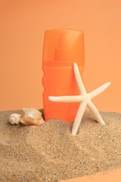 Sand with bottle of sunscreen, starfish and seashells against orange background. Sun protection