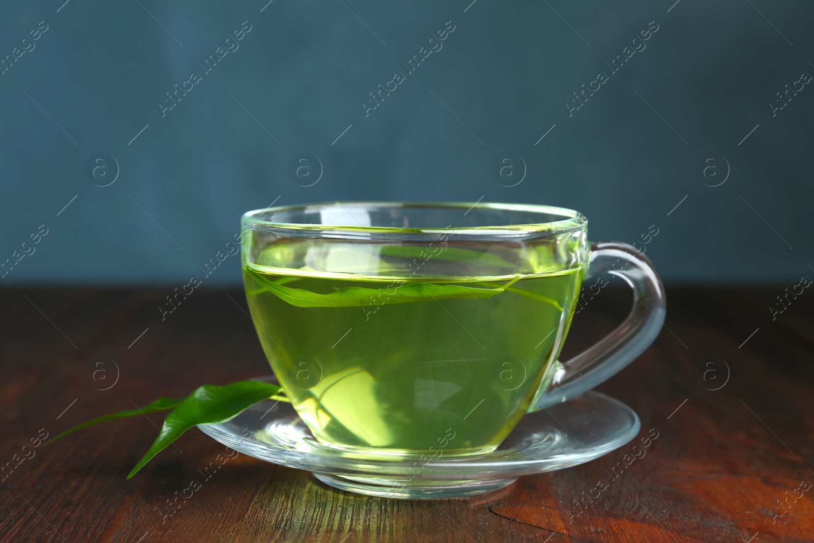 Photo of Cup of aromatic green tea and leaves on wooden table