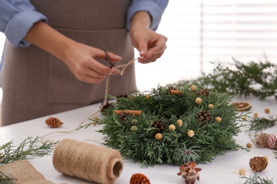 Photo of Florist making beautiful Christmas wreath at white wooden table indoors, closeup