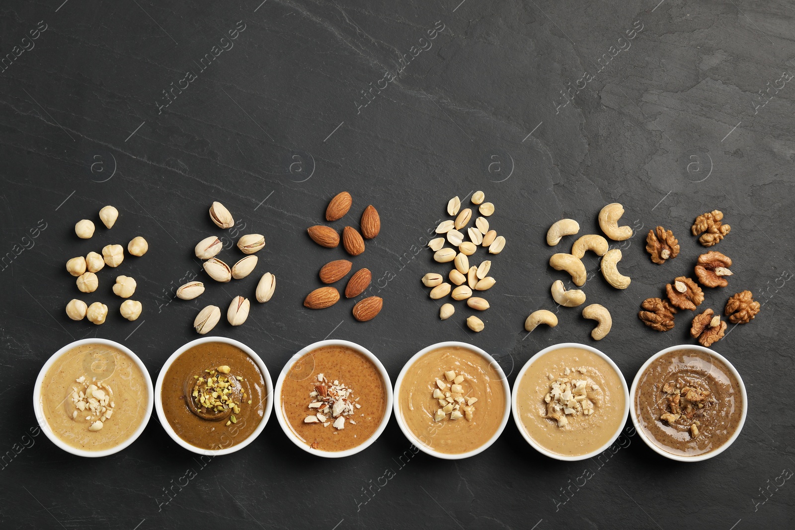 Photo of Tasty nut butters in bowls and raw nuts on black table, flat lay