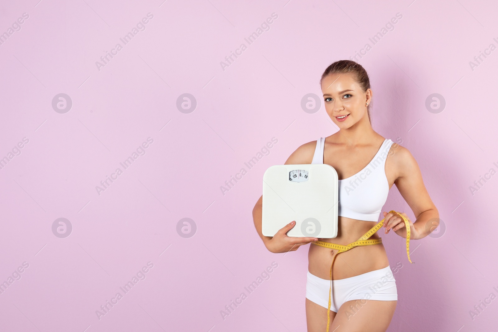 Photo of Beautiful young woman with scales and measuring tape on color background. Healthy diet