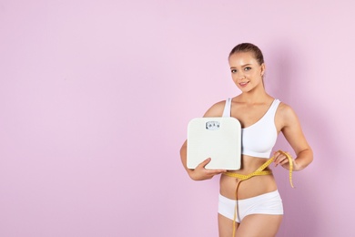 Photo of Beautiful young woman with scales and measuring tape on color background. Healthy diet