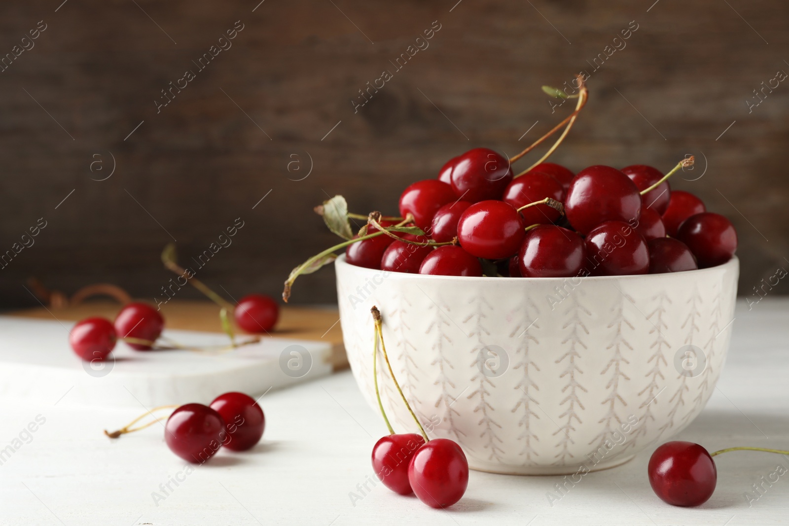 Photo of Bowl of delicious cherries on white table against wooden wall, space for text