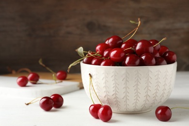 Photo of Bowl of delicious cherries on white table against wooden wall, space for text