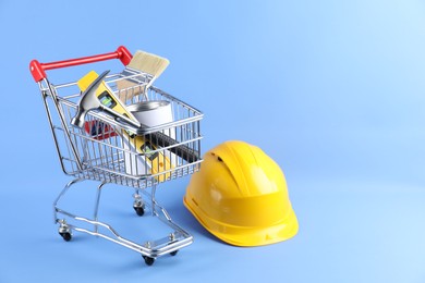 Photo of Small shopping cart with set of construction tools and hard hat on color background