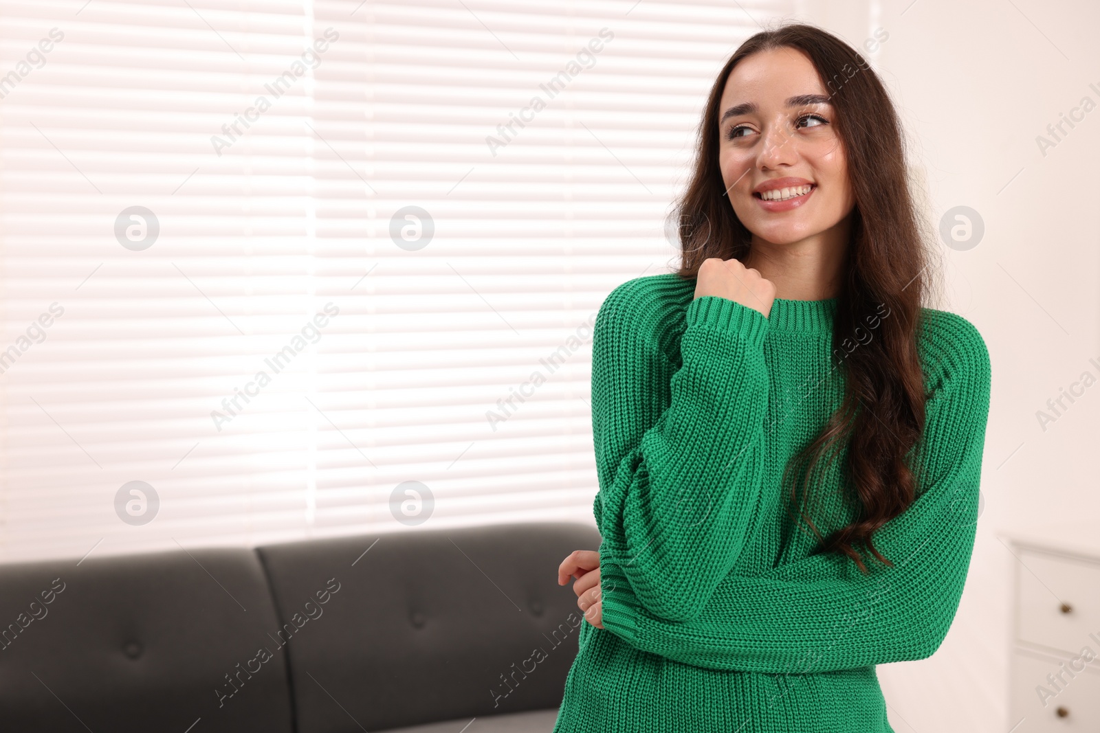 Photo of Beautiful young woman in stylish warm sweater at home, space for text