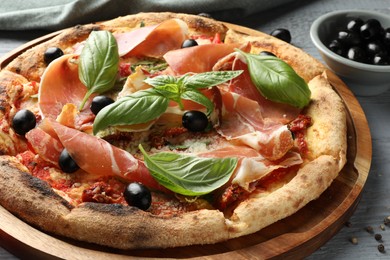 Photo of Tasty pizza with cured ham, olives, sun-dried tomato and basil on gray table, closeup