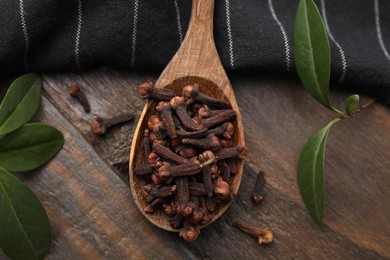 Photo of Spoon with aromatic cloves and green leaves on wooden table, flat lay