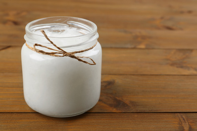 Photo of Organic coconut oil in jar on wooden table, space for text. Healthy cooking