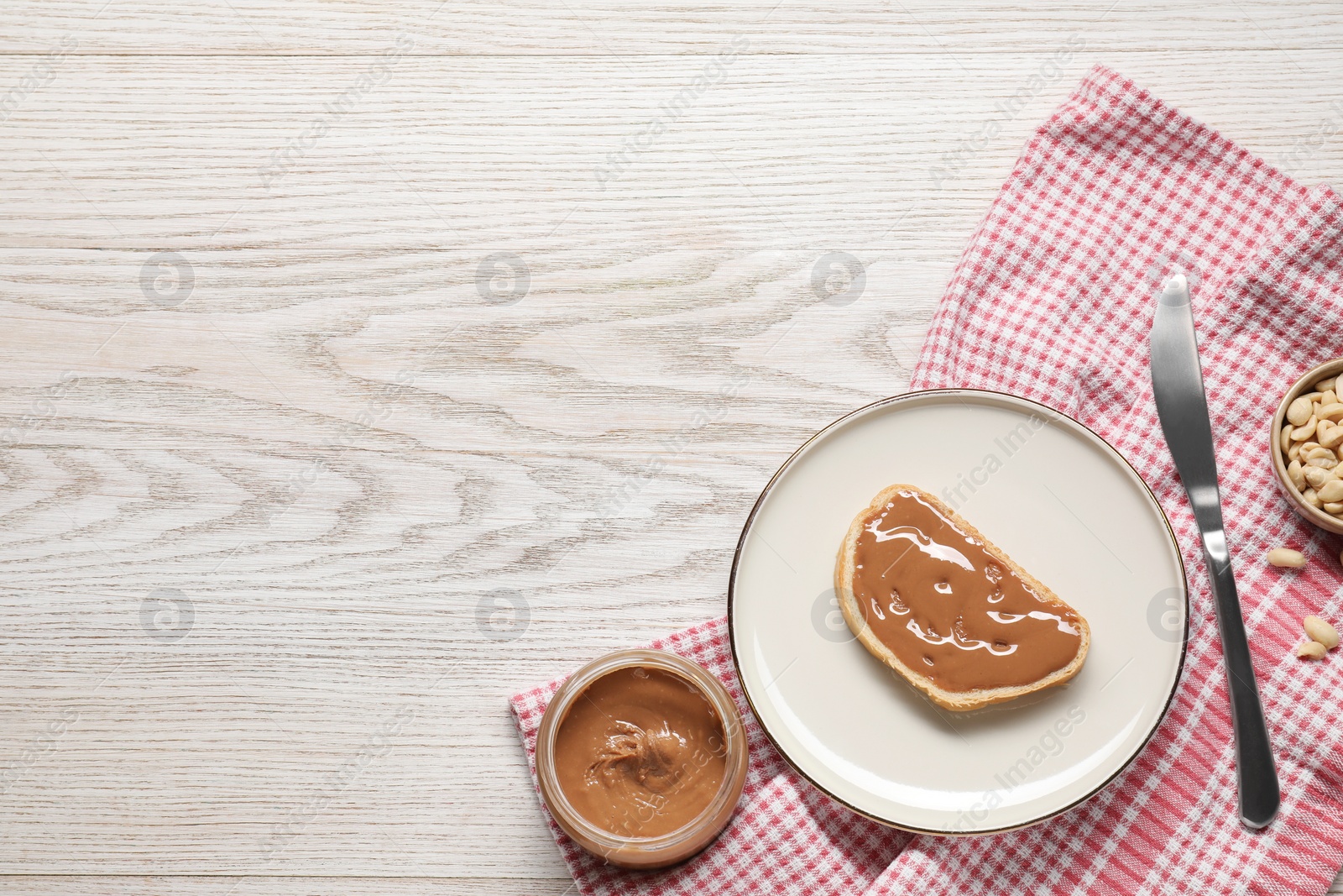 Photo of Toast with tasty nut butter and knife on white wooden table, flat lay. Space for text