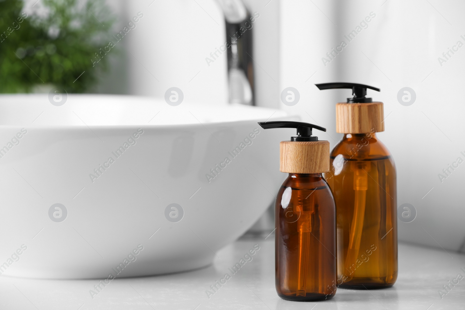 Photo of Bottles with dispenser caps on white table in bathroom. Space for text