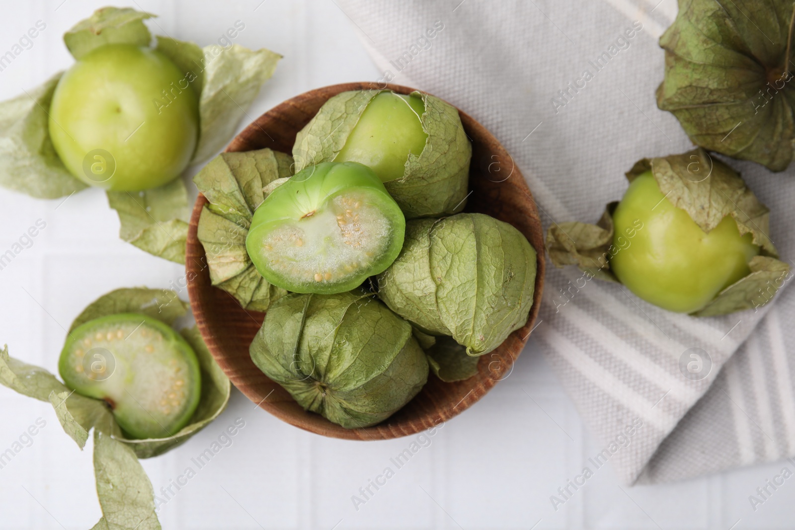 Photo of Fresh green tomatillos with husk in bowl on white table, flat lay