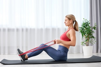 Photo of Fit woman doing exercise with fitness elastic band on mat at home