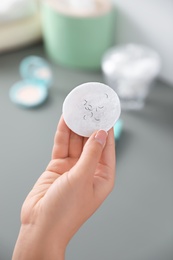 Young woman holding cotton pad with fallen eyelashes indoors