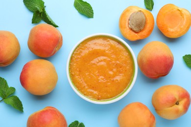 Photo of Apricot puree in bowl and fresh fruits with mint on light blue background, flat lay