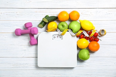 Photo of Flat lay composition with scales, healthy food, measuring tape and dumbbells on wooden background. Weight loss