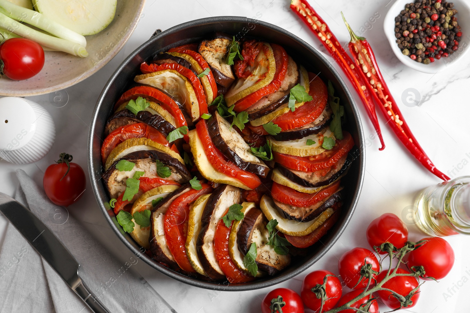 Photo of Delicious ratatouille, ingredients and knife on white table, flat lay