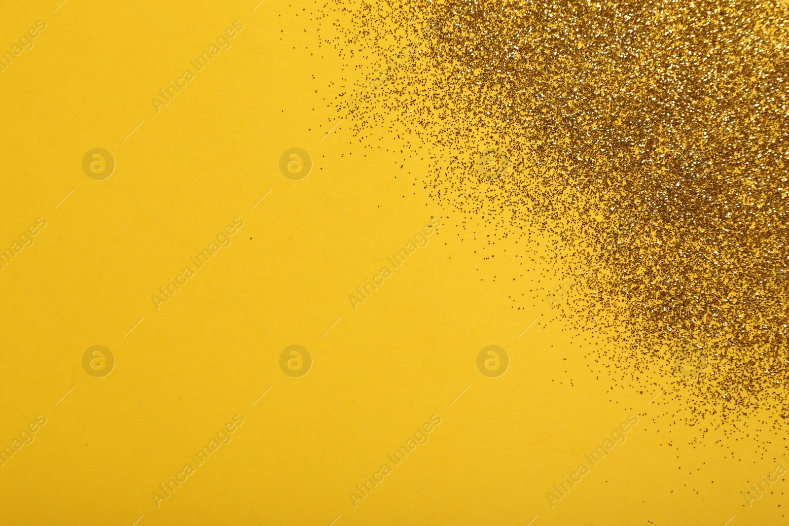 Photo of Shiny golden glitter on yellow background, top view. Space for text