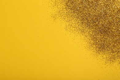 Shiny golden glitter on yellow background, top view. Space for text