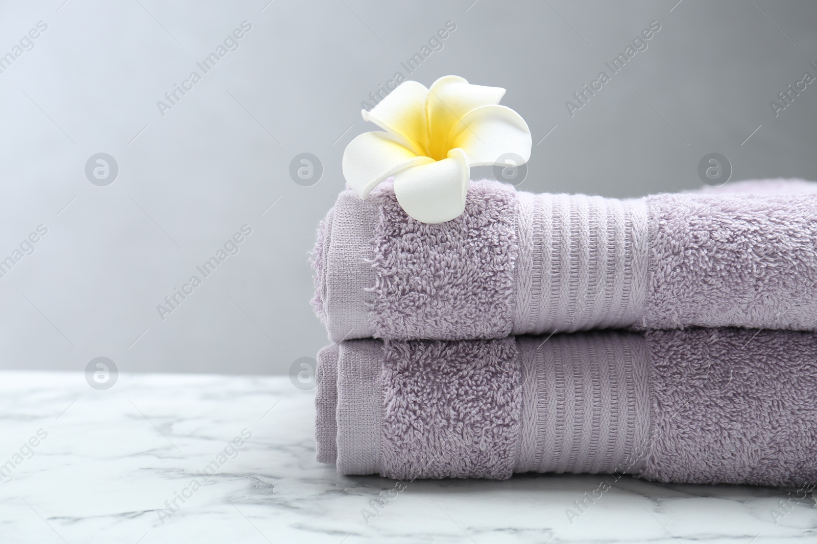 Photo of Violet terry towels and plumeria flower on white marble table, closeup. Space for text