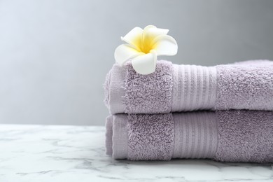 Violet terry towels and plumeria flower on white marble table, closeup. Space for text