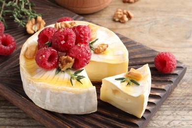 Photo of Brie cheese served with raspberries, walnuts and honey on wooden table