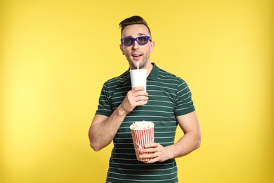 Photo of Man with 3D glasses, popcorn and beverage during cinema show on color background