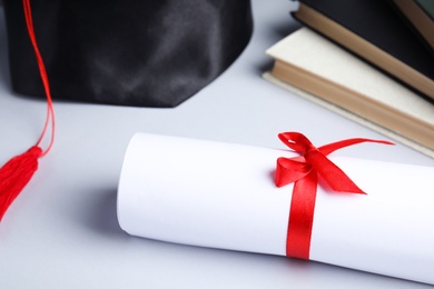 Graduation hat, books and student's diploma on white background