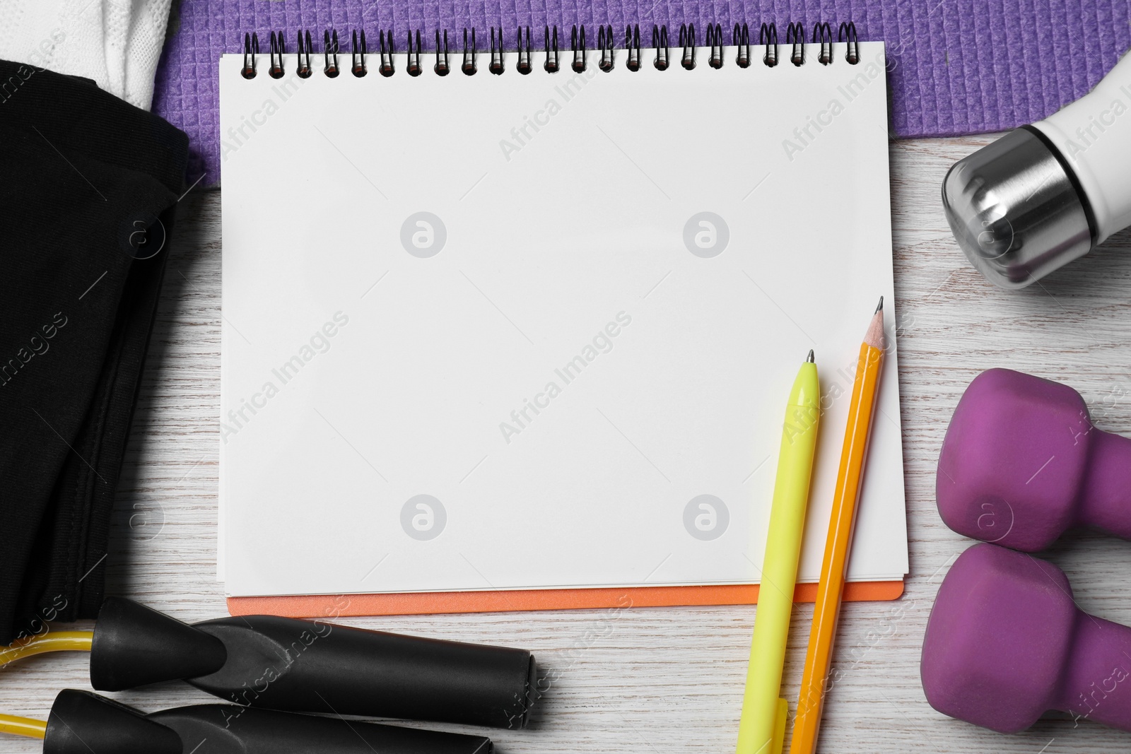 Photo of Notebook surrounded by sports equipment on white wooden table, flat lay. Personal training