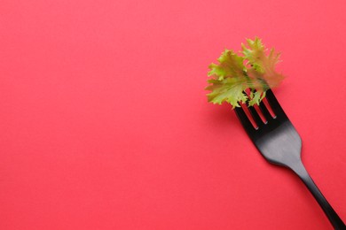 Fork with lettuce leaf on red background, top view and space for text. Diet concept