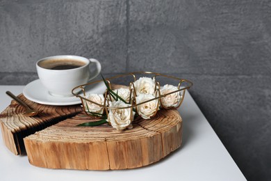 Photo of Decorative gold holder with flowers and cup of coffee on white table. Interior design