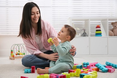 Cute baby boy playing with mother and building blocks on floor at home