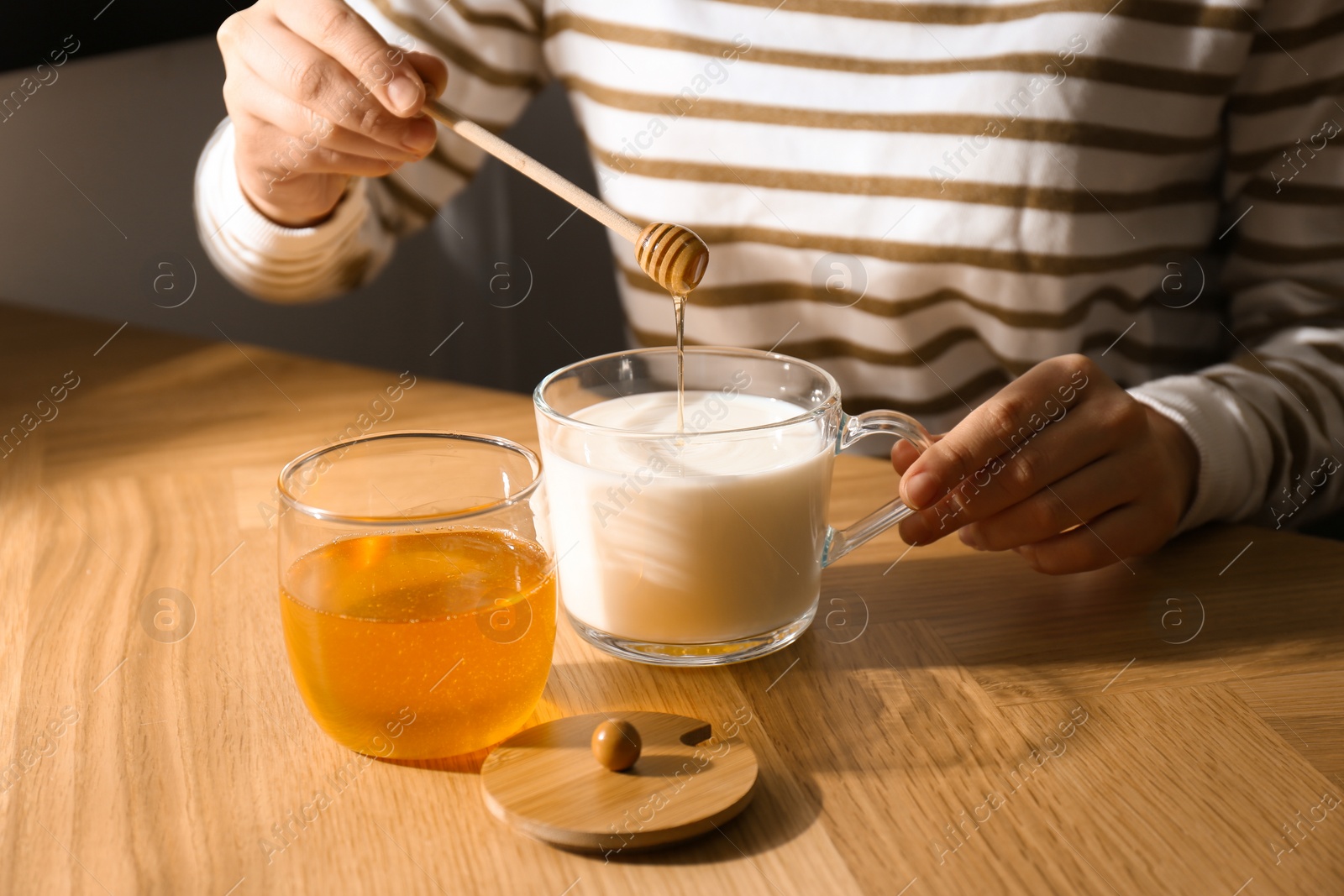 Photo of Woman adding honey to milk at wooden table closeup