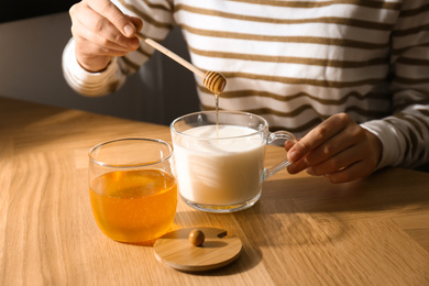 Woman adding honey to milk at wooden table closeup