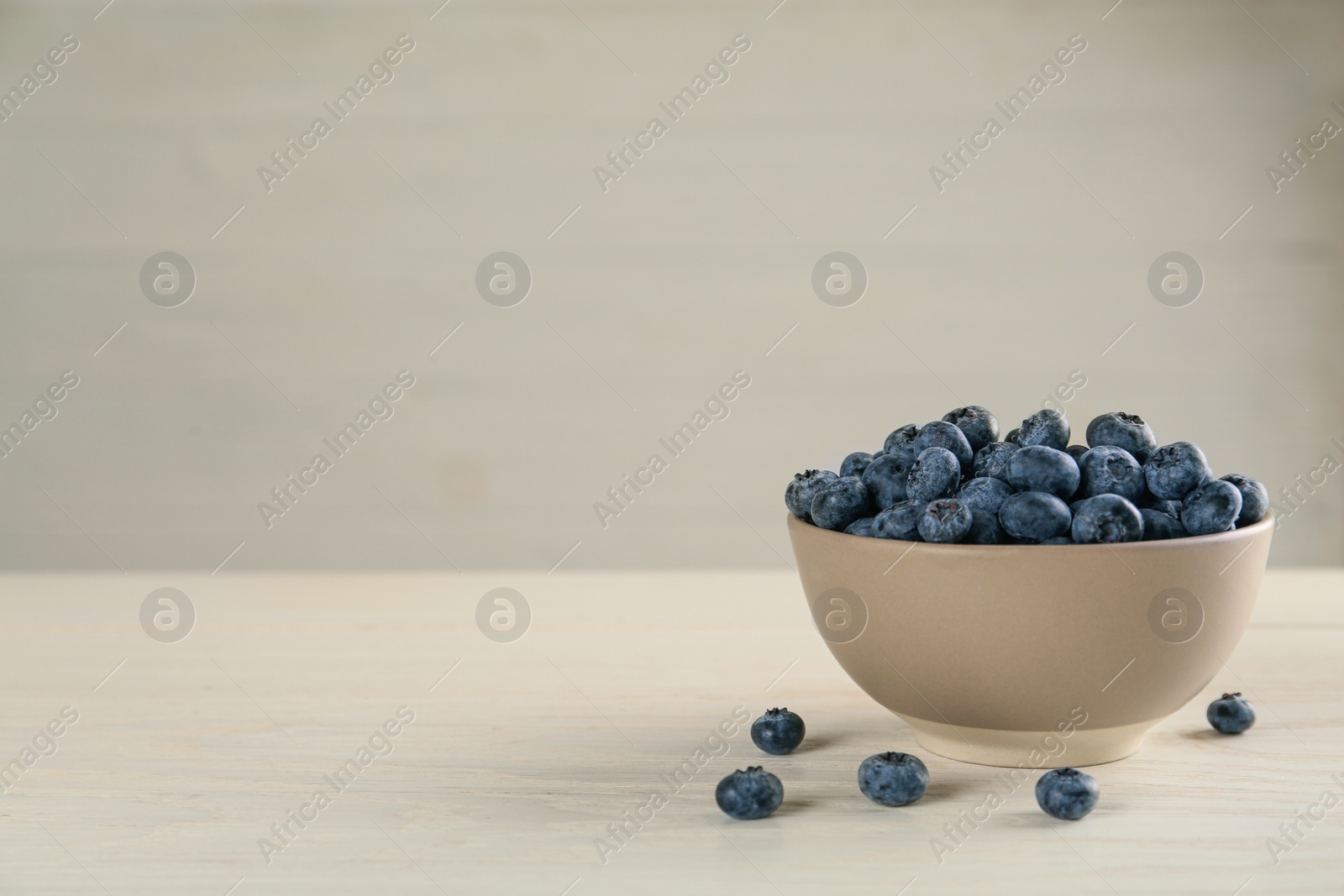 Photo of Ceramic bowl with blueberries on light wooden table, space for text. Cooking utensil