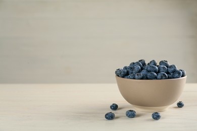 Ceramic bowl with blueberries on light wooden table, space for text. Cooking utensil