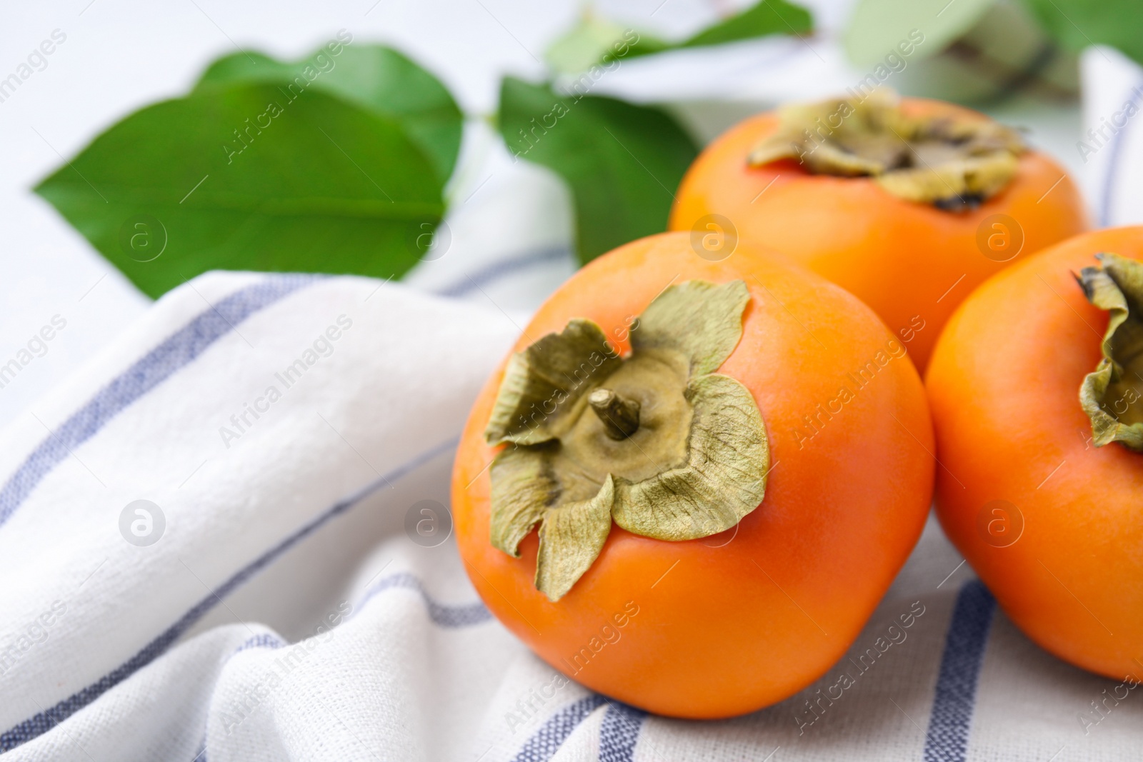 Photo of Delicious ripe juicy persimmons on striped cloth, closeup