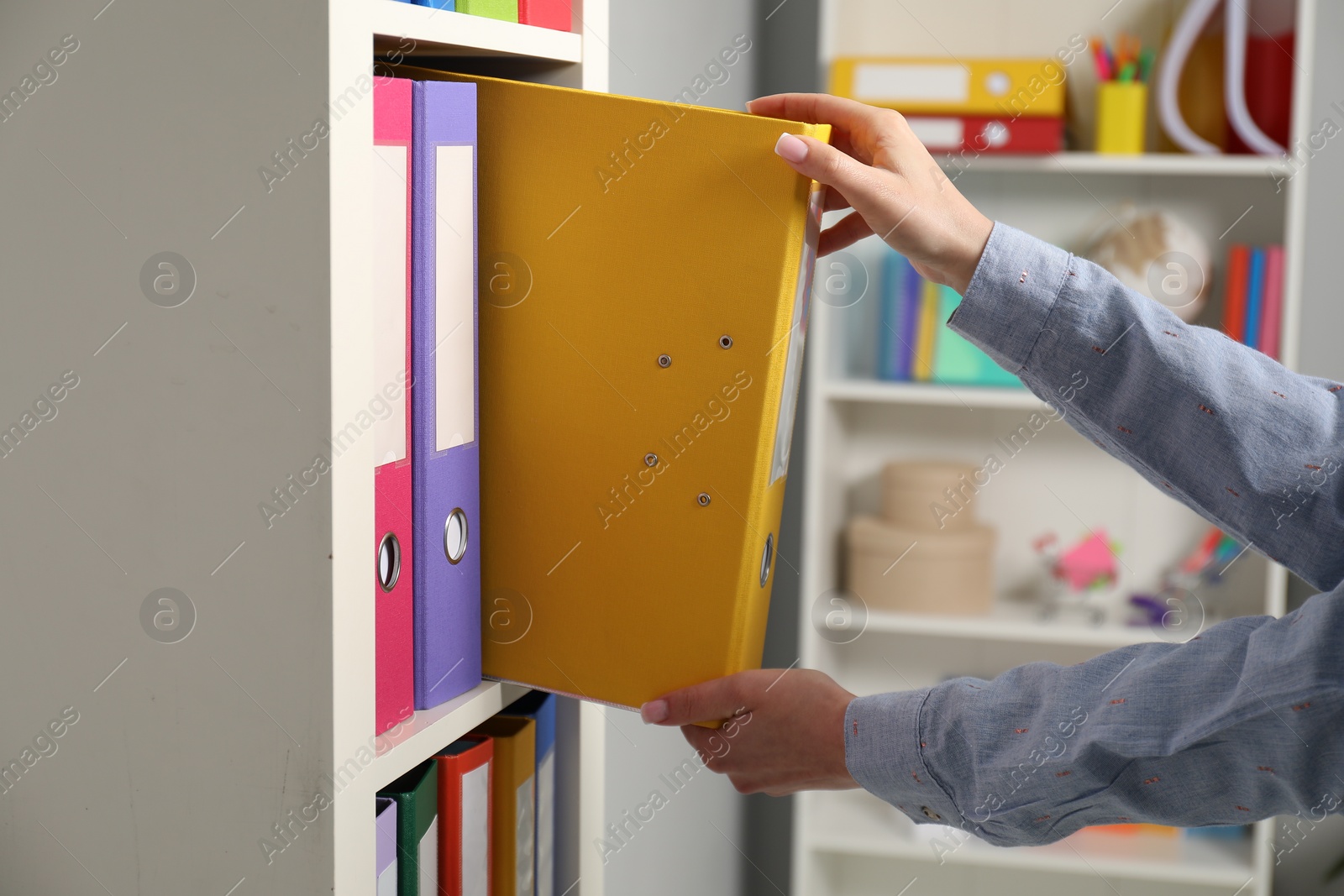 Photo of Woman taking binder office folder from shelving unit indoors, closeup