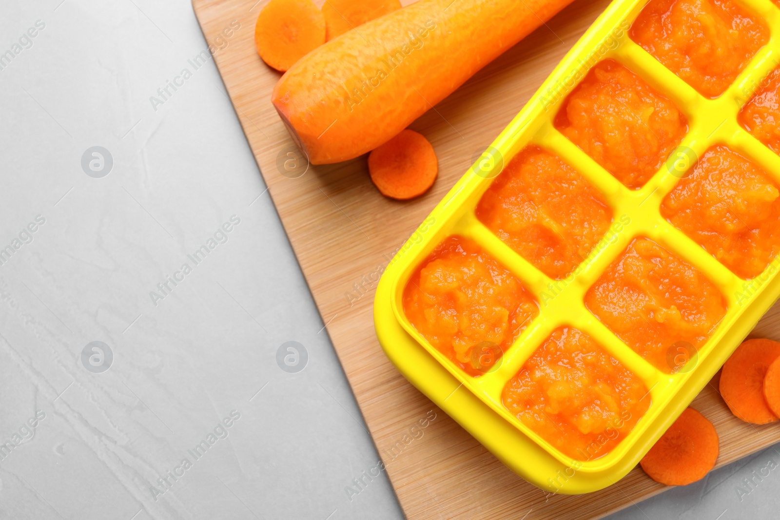 Photo of Carrot puree in ice cube tray ready for freezing on light grey table, flat lay. Space for text
